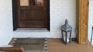 A wooden door with a dark frame, a white brick wall, a welcome mat, and a lantern on the porch. - Welcome to our home! Lakefront Living, Where Beautiful Sunsets are unforgettable (Lake Park)