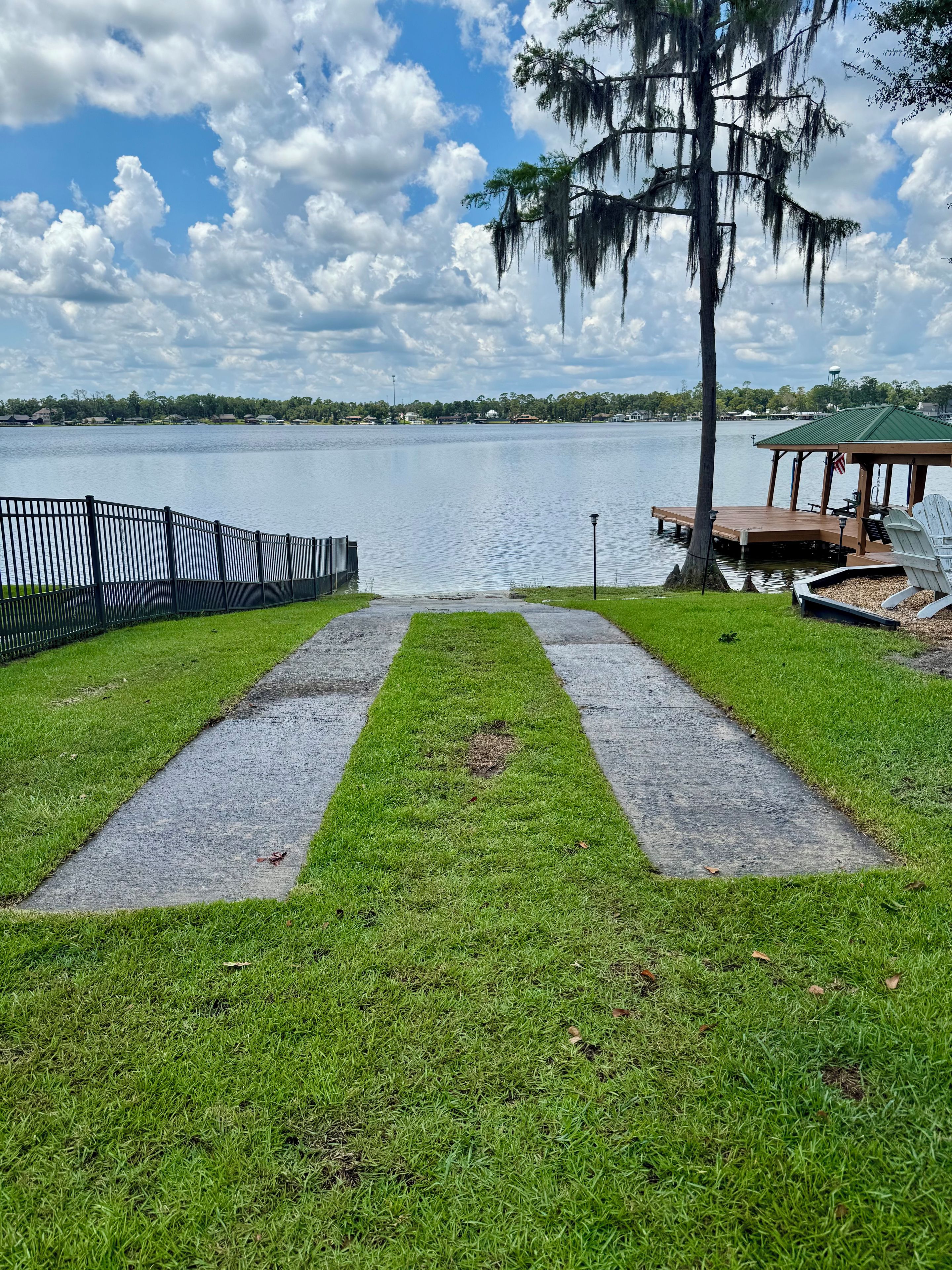 Polku johtaa laiturille, jossa on katettu huvimaja ja tuoleja. Laiturilta avautuu näkymä tyyneen järveen ja kirkkaalle taivaalle.