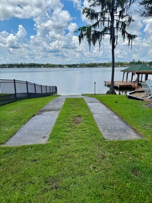A pathway leading to a dock with a gazebo and chairs, overlooking a calm lake with a clear sky.