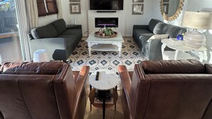 A living room with a ceiling fan, a flat-screen TV, a fireplace, and a large mirror. - Welcome to our home! Lakefront Living, Where Beautiful Sunsets are unforgettable (Lake Park)