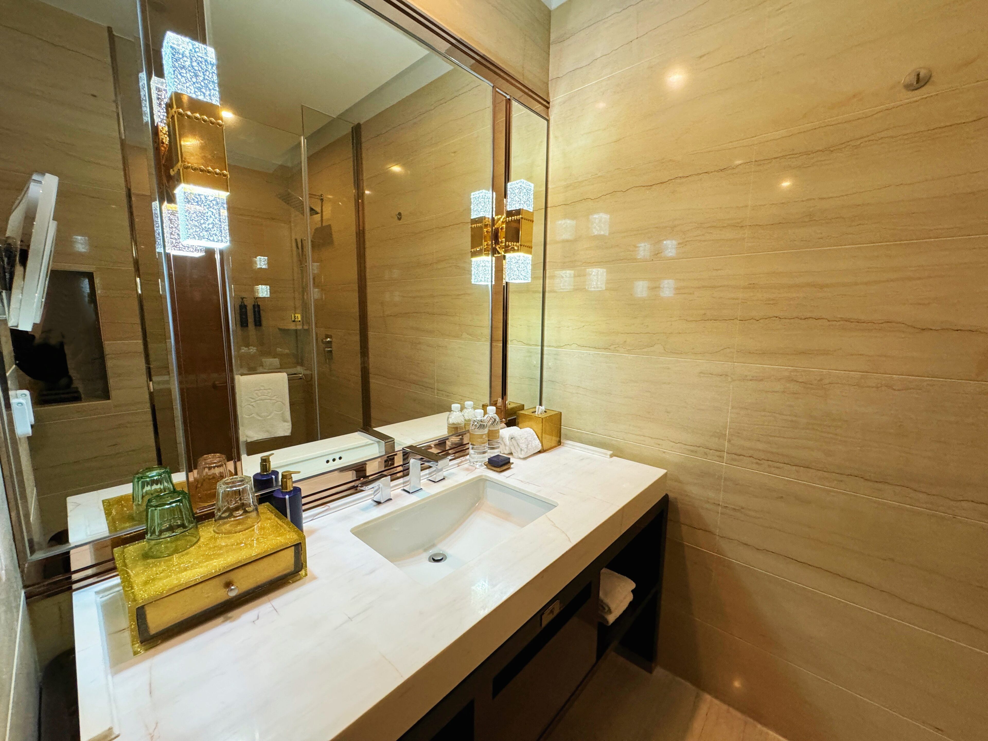 A modern bathroom with a large mirror, a white sink, and a vanity with toiletries.