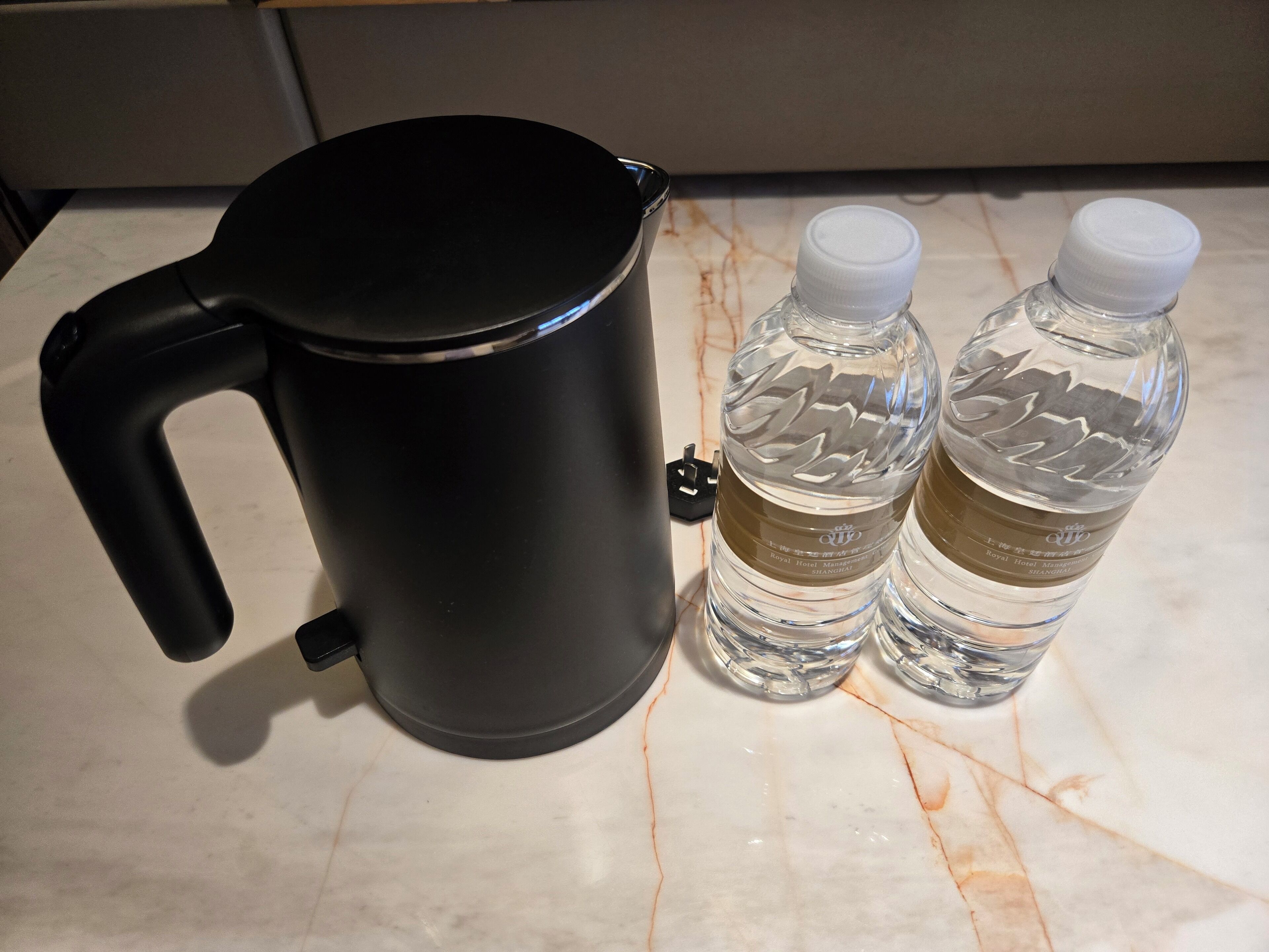 Una tetera eléctrica negra y dos botellas de agua sobre una encimera de mármol.