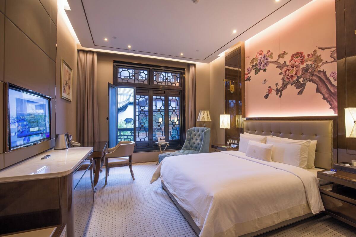 Une chambre d’hôtel équipée d’un lit, d’un bureau, d’une chaise, d’une télévision et d’une grande fenêtre donnant sur un beau paysage.