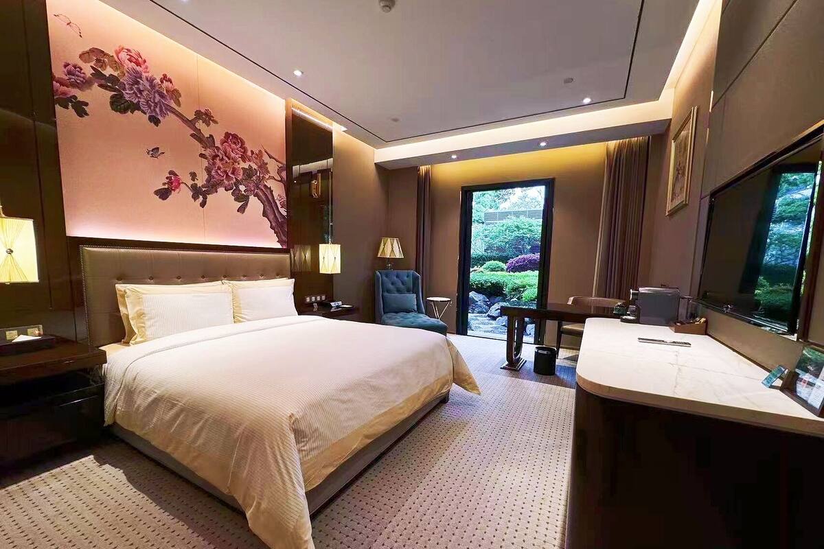 Une chambre d’hôtel avec un grand lit, un bureau, une chaise, une télévision et une vue sur un jardin.