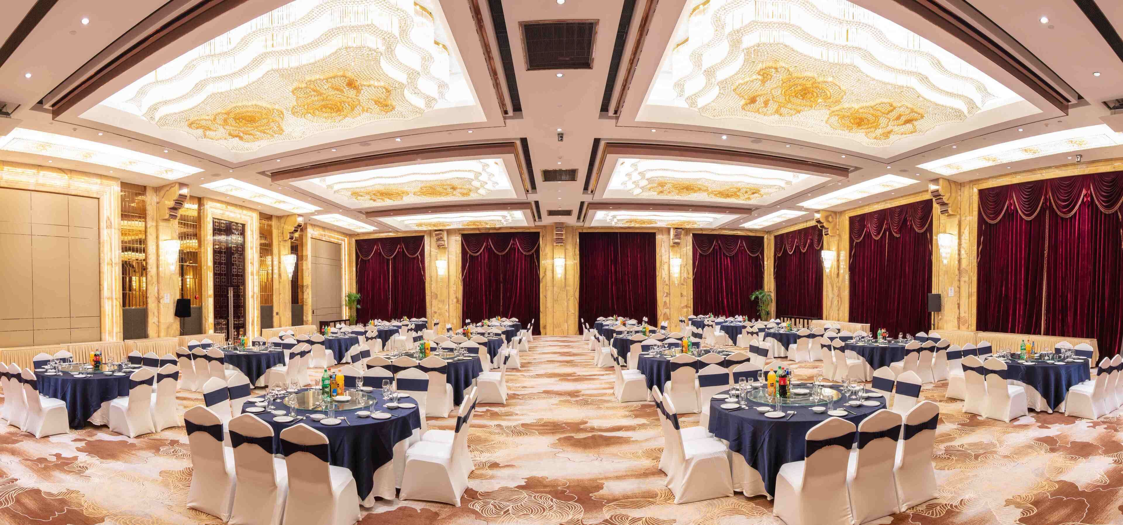 Uma sala de banquetes com mesas redondas preparadas para refeições, cada uma com cadeiras brancas e toalhas de mesa azul-marinho.
