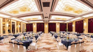 Uma sala de banquetes com mesas redondas preparadas para refeições, cada uma com cadeiras brancas e toalhas de mesa azul-marinho.