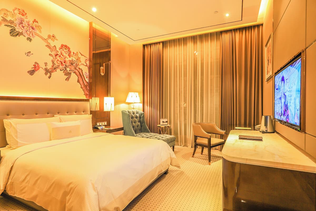 A hotel room with a large bed, a desk, a chair, a TV, and a wall with a floral mural.