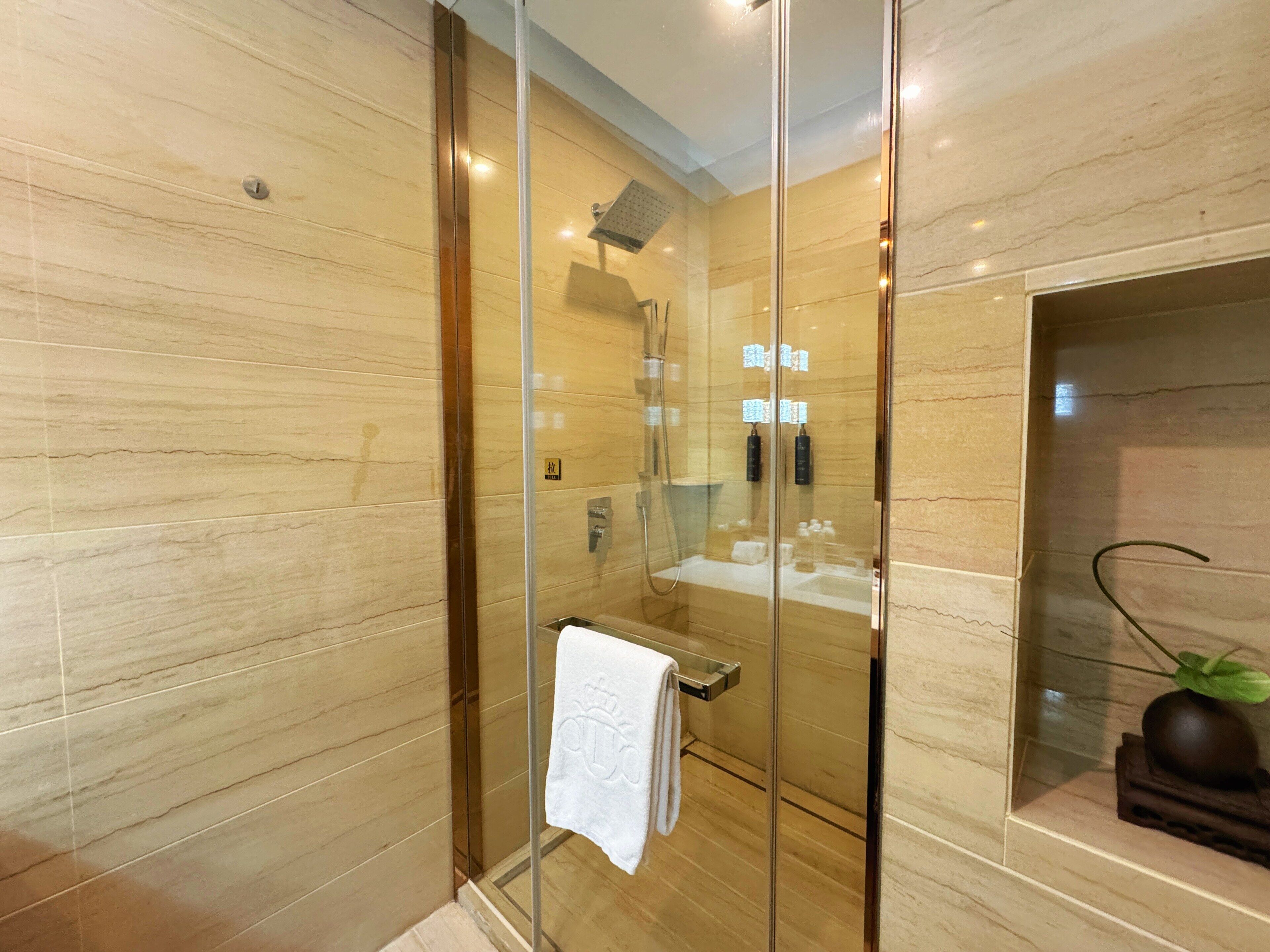 Een moderne badkamer met een douchecabine van glas, een glazen scherm en een wastafel met spiegel en handdoekhouder.