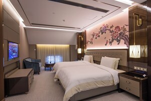 Una camera d'albergo moderna con un letto grande, una televisione, una scrivania e un murale decorativo.