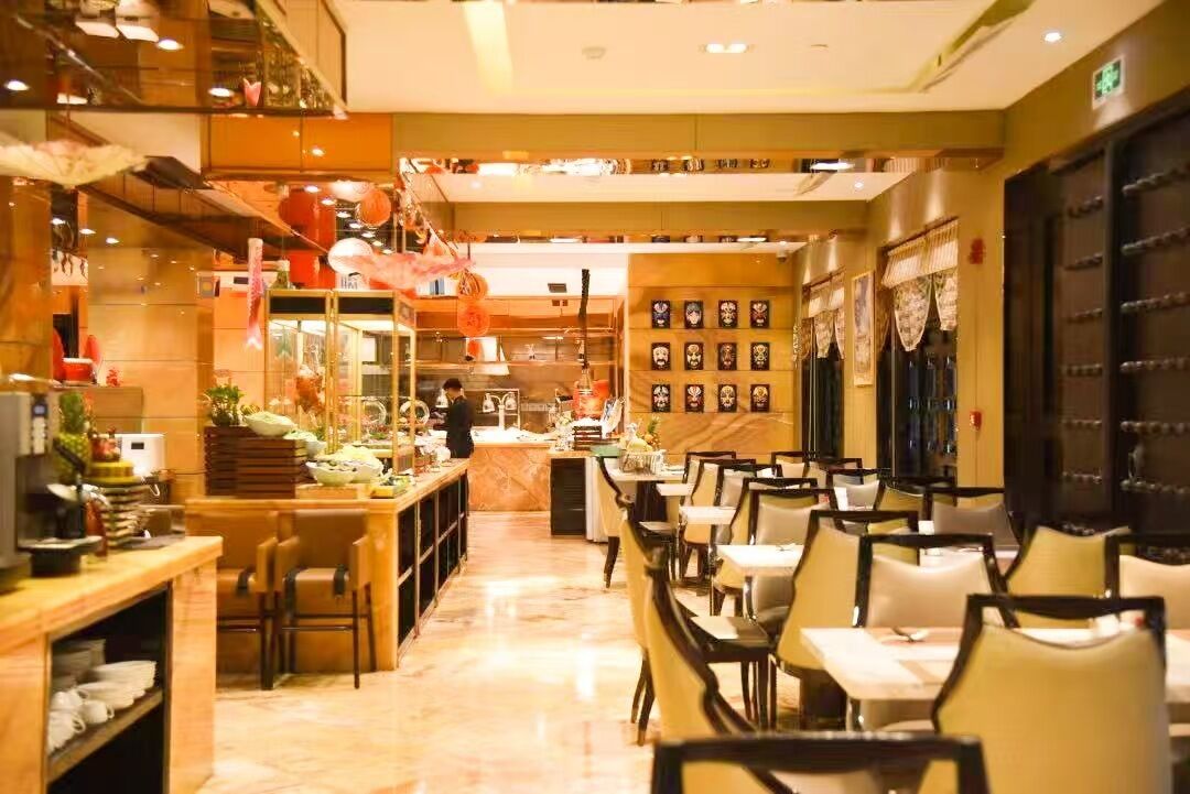 Un restaurante con una barra larga, varias mesas y sillas. Hay elementos decorativos y una persona trabajando detrás de la barra.