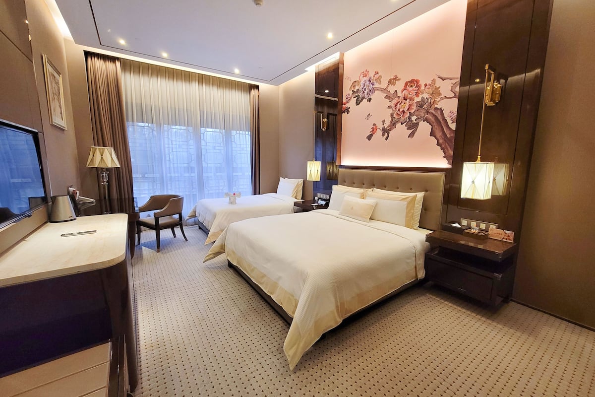 Une chambre d’hôtel avec deux lits, un bureau, une chaise, une télévision et un mur décoratif.