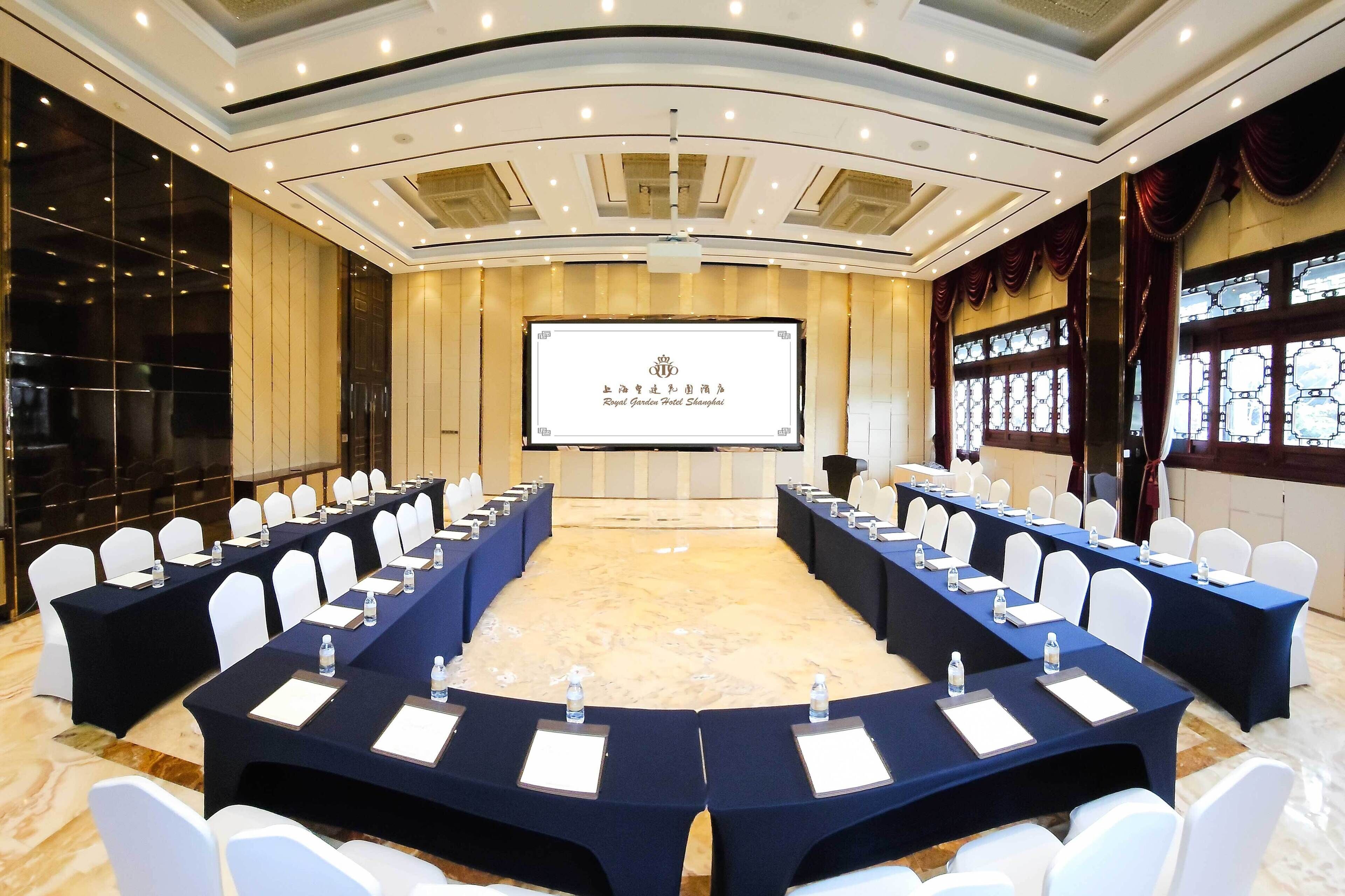 Une salle de conférence avec une longue table, des chaises blanches et un écran de projection affichant du texte.