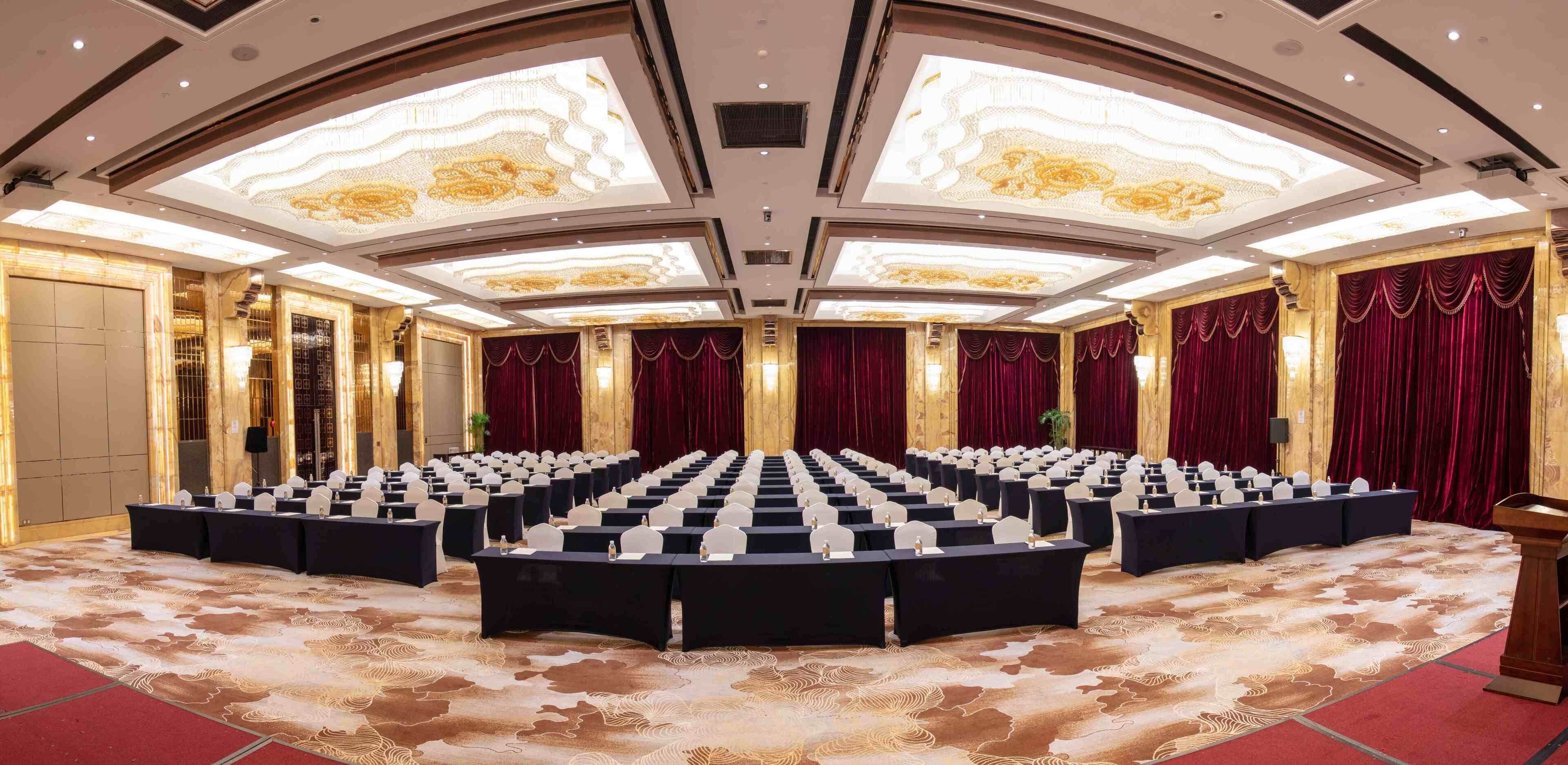 A conference room with rows of tables and chairs, a podium, and a patterned carpet.