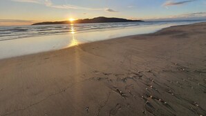 Ein Strand bei Sonnenuntergang, ruhiges Wasser und eine entfernte Insel.