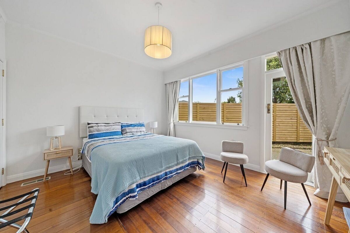 Une chambre à coucher avec un grand lit, une table de chevet avec une lampe, une chaise et une fenêtre avec des rideaux.