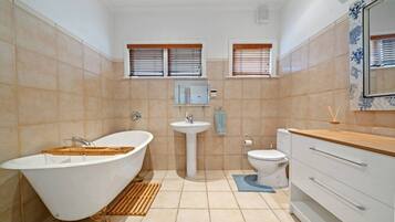A bathroom with a freestanding bathtub, a pedestal sink, a toilet, and a vanity with drawers.