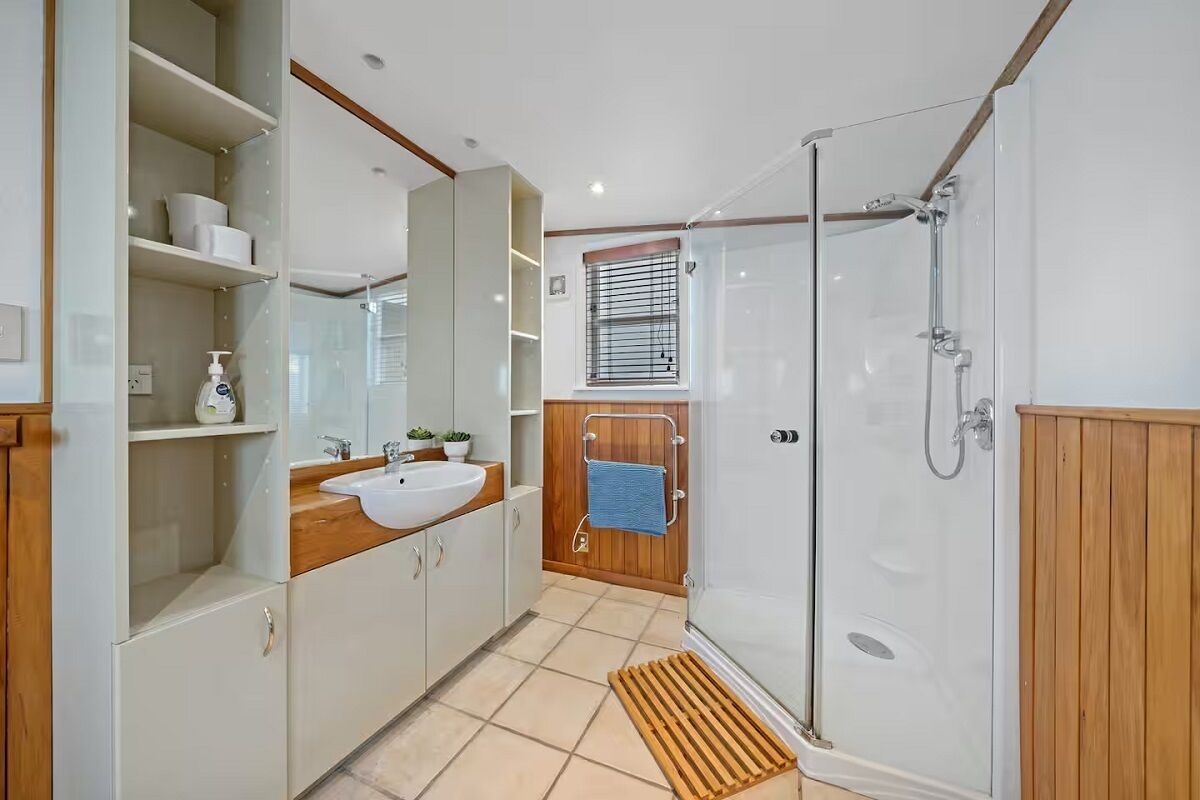 Un baño moderno con cabina de ducha de vidrio, tocador de madera, lavabo y espejo.