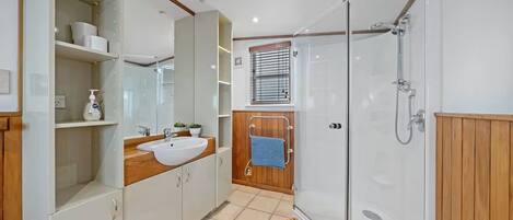 Un baño moderno con cabina de ducha de vidrio, tocador de madera, lavabo y espejo.