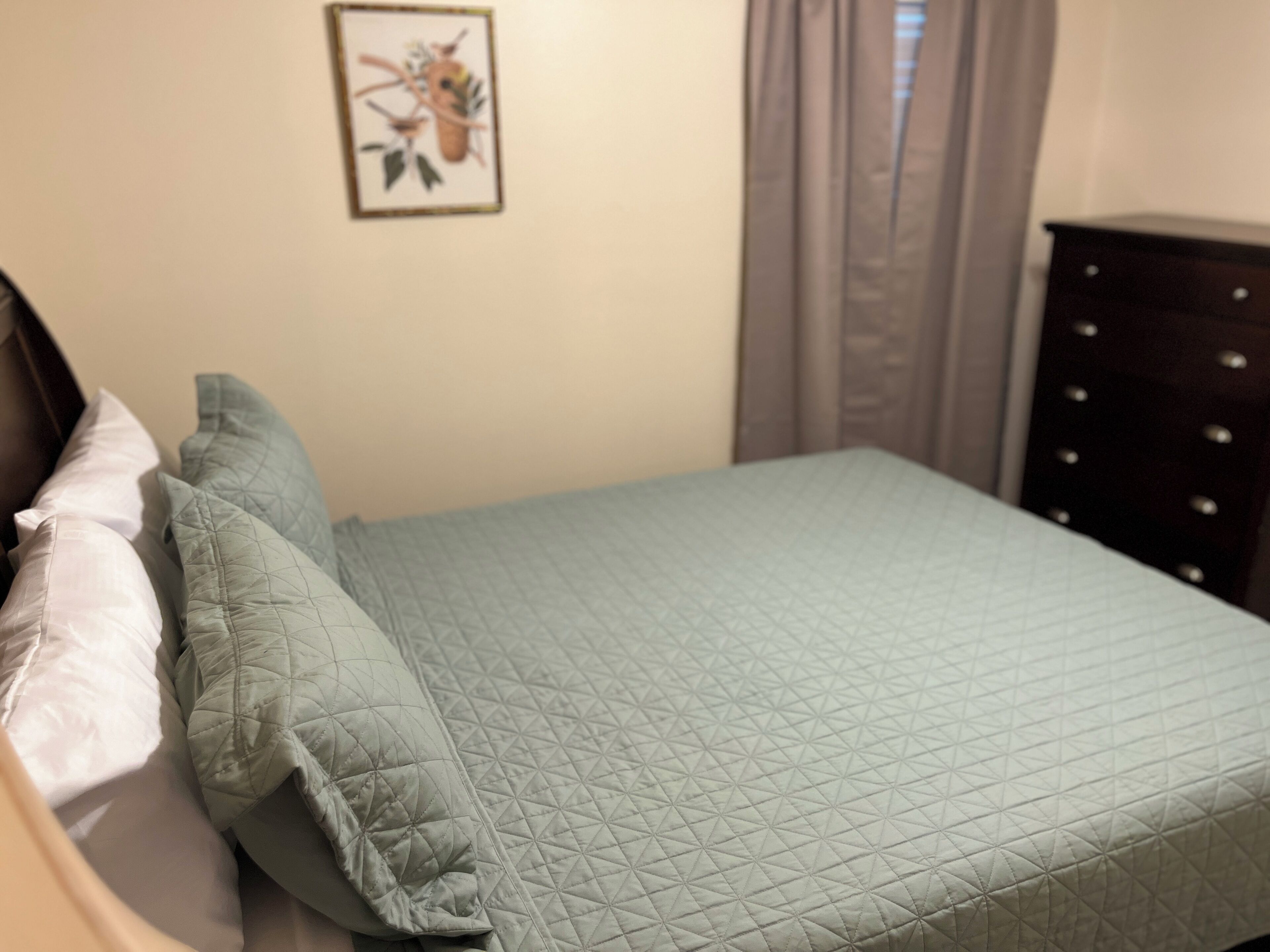 A bed with a quilted cover, a white pillow, and a dark wooden dresser with drawers.