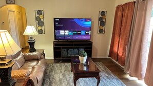 A living room with a leather sofa, a coffee table, a TV on a stand, and a lamp.