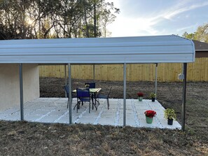 Un patio couvert avec une table et des chaises, entouré d’une clôture en bois et agrémenté de plantes en pot.