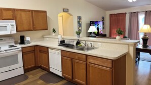 A modern kitchen with wooden cabinets, a white stove, and a built-in dishwasher. There is a small island with a sink and a ceiling fan above.