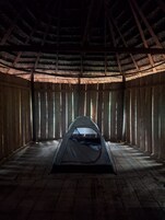 Una tienda de campaña montada dentro de una estructura de madera con techo de paja, ventanas grandes y paredes de madera.