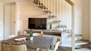 A modern kitchen with a built-in stove, a dining table with chairs, and a staircase with a minimalist design. - La Breva by Interhome (Domaso)