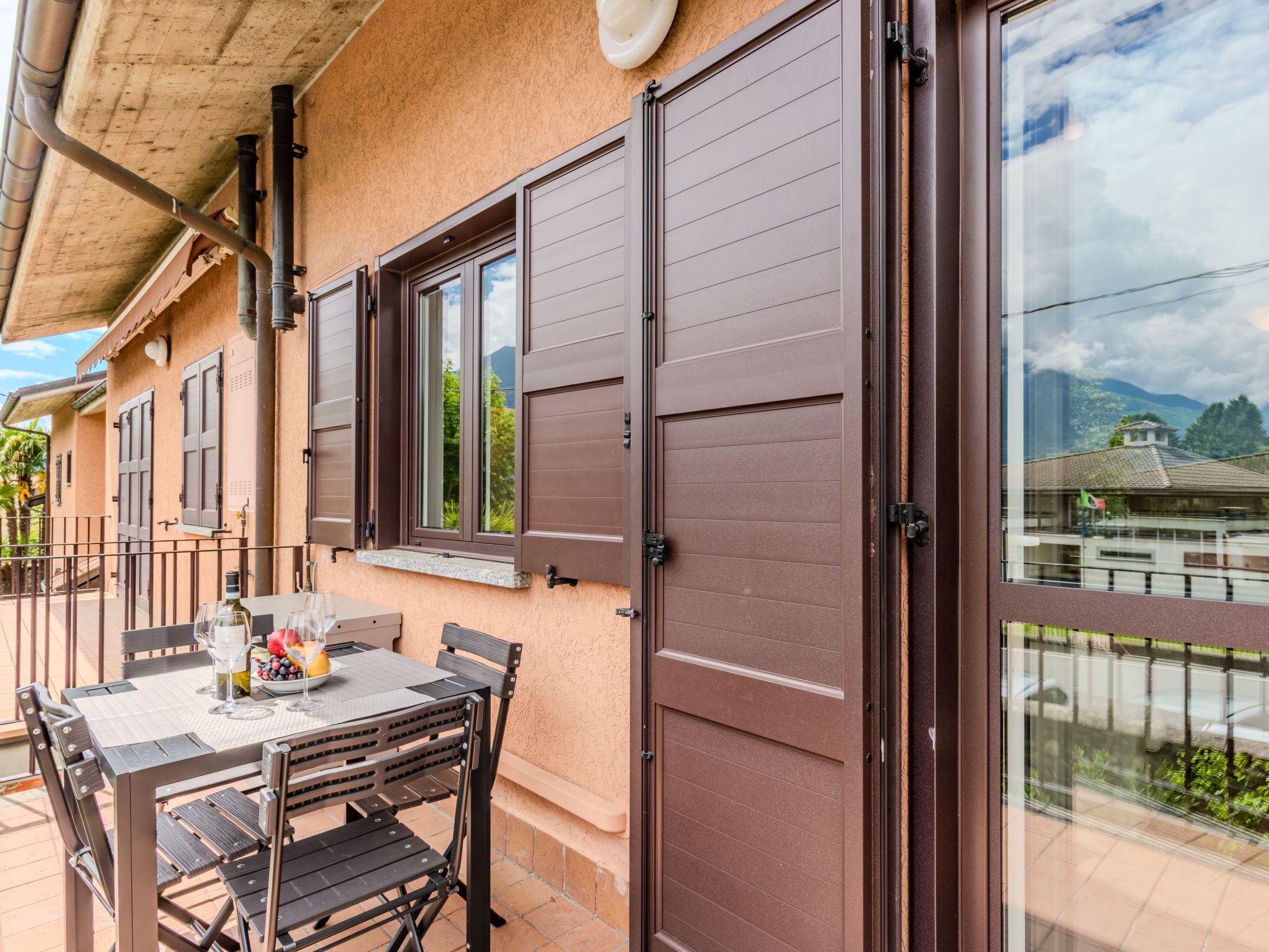Un patio con una mesa y sillas, una ventana con contraventanas marrones y vista a un edificio con una bandera.