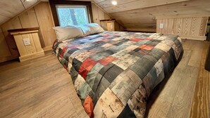 Un dormitorio con techo de madera, una cama grande con colcha colorida, una ventana y un aparador de madera.