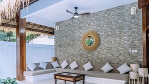 Un espace de vie moderne comprenant un ensemble de canapés, une table basse en verre, un ventilateur de plafond et un élément décoratif mural.