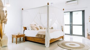 Une chambre à coucher avec un lit à baldaquin, une table de chevet, un tapis rond en fibres naturelles et une grande fenêtre donnant sur un beau paysage.