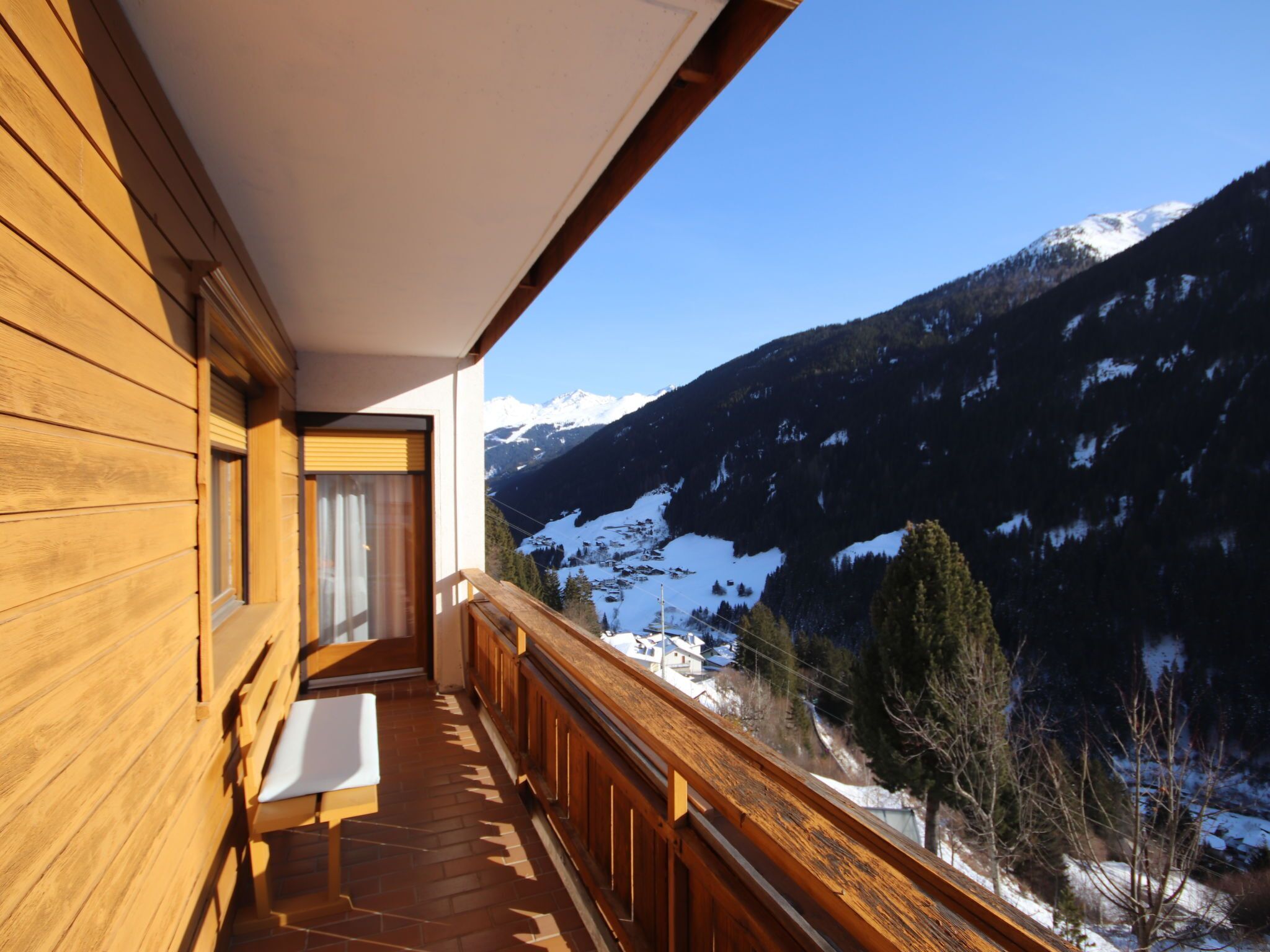 A wooden balcony with a view of snow-capped mountains and a clear sky.