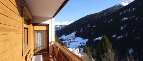 A wooden balcony with a view of snow-capped mountains and a clear sky.