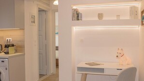 Une cuisine moderne équipée d’un lave-linge, d’une petite table ornée d’une statuette de chat et d’une bibliothèque contenant des livres et des objets décoratifs.