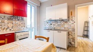 A compact kitchen with red cabinets, a white stove, and patterned tile backsplash. - Maurizio's Place by Interhome (Ceriale)