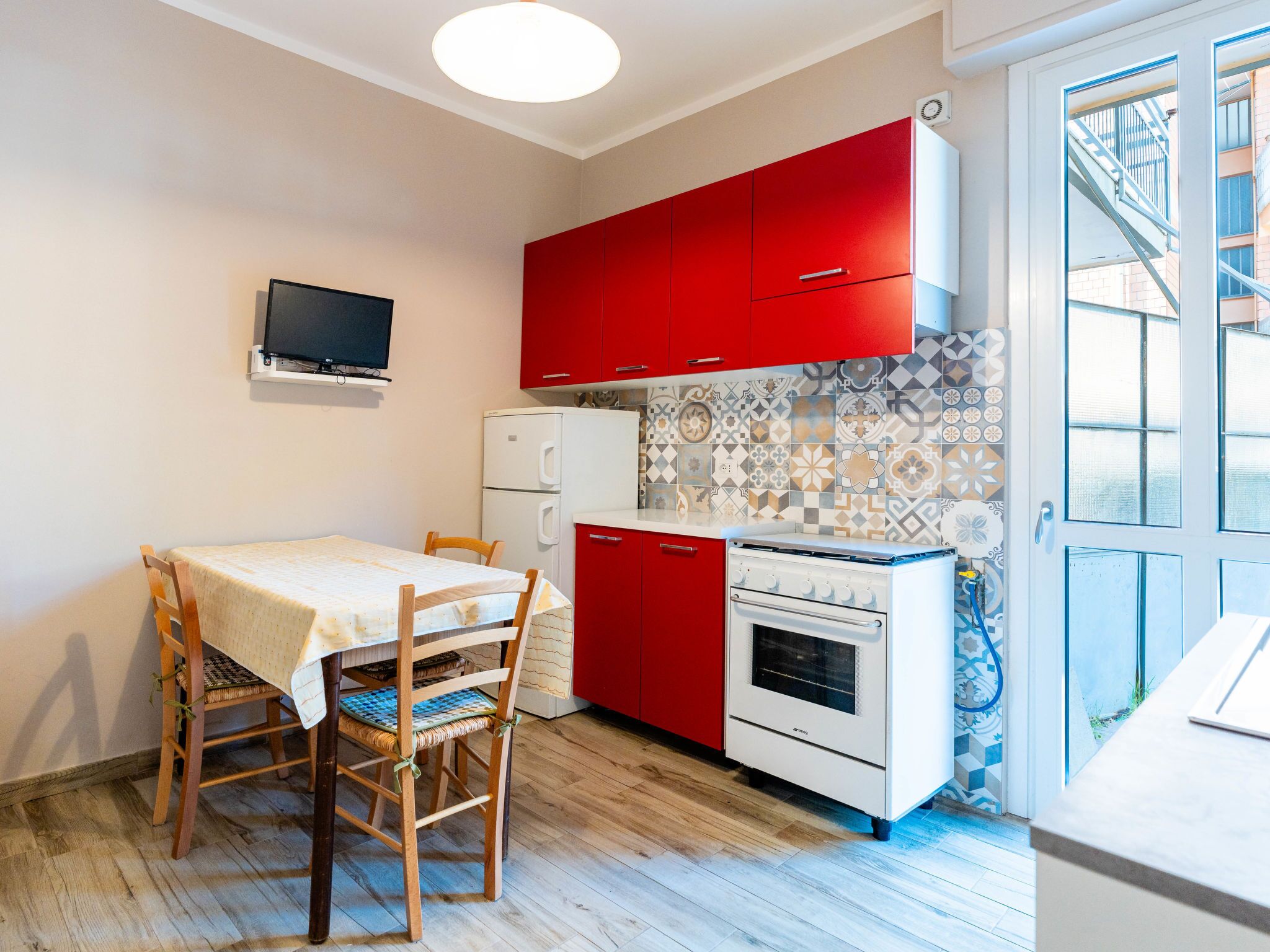 Une cuisine de taille réduite avec des meubles rouges, un réfrigérateur blanc et un pare-feu en carrelage.