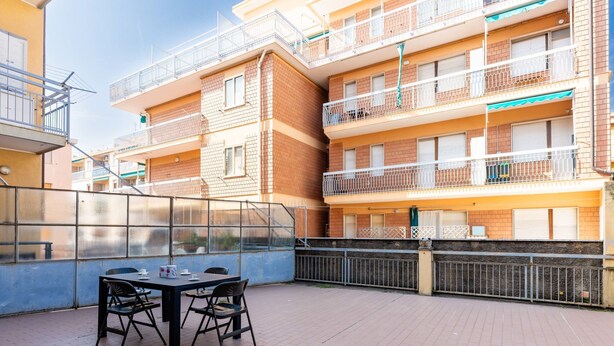A terrace with a table and chairs, a glass partition, and a view of multi-story buildings with balconies. - Maurizio's Place by Interhome (Ceriale)