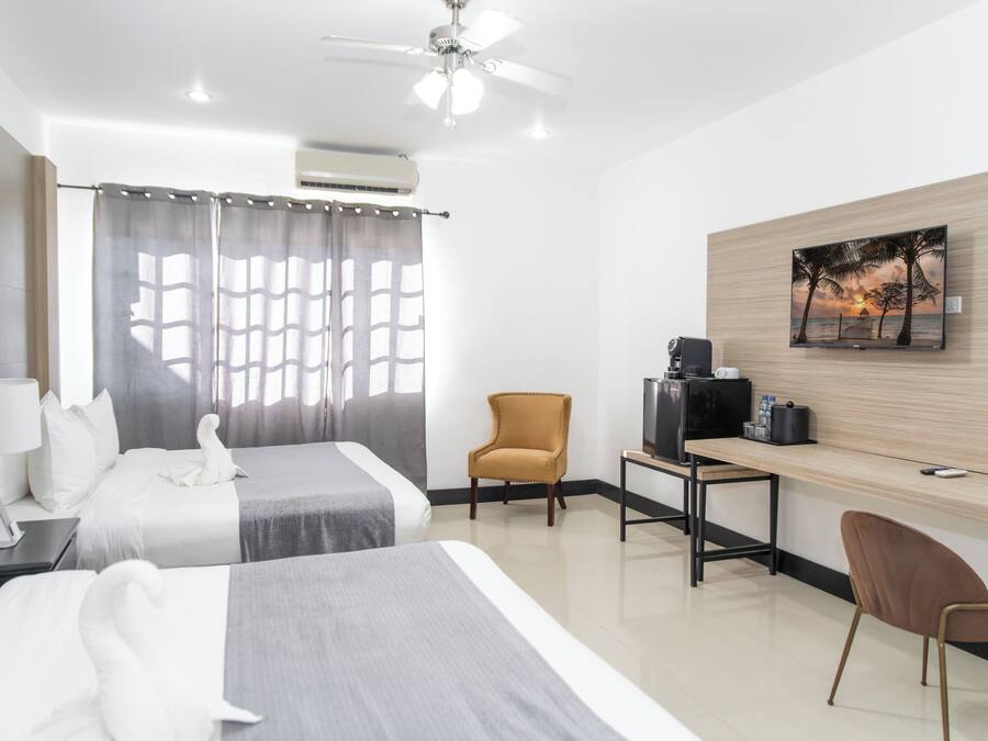 Habitación de hotel con dos camas, un escritorio con computadora, una silla, un televisor y un cuadro en la pared.