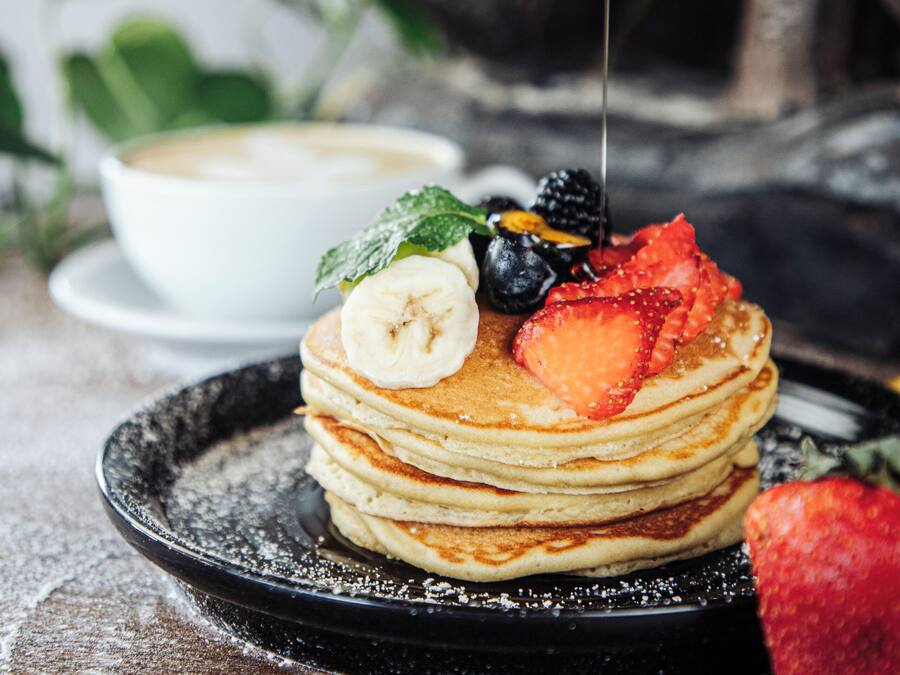 A stack of pancakes with fruit toppings and syrup on a black plate.
