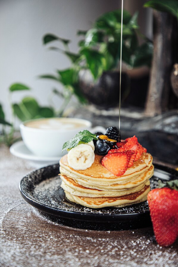 A stack of pancakes with fruit toppings and syrup on a black plate.