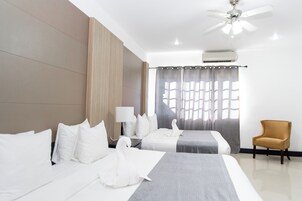 Habitación de hotel con dos camas, ventilador de techo, aire acondicionado, lámpara, una silla y ventana con cortinas.