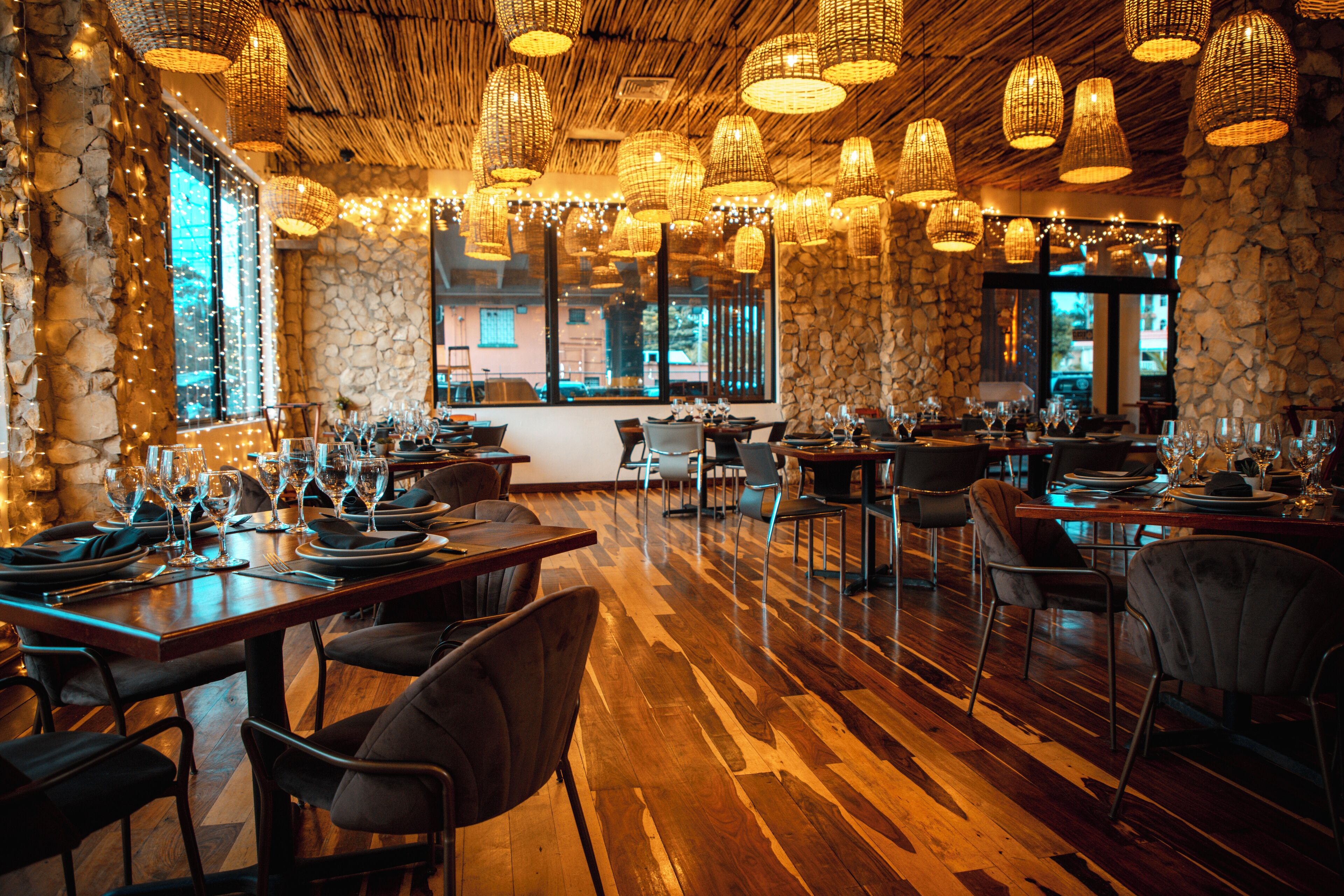 A restaurant with wooden flooring, stone walls, and multiple tables set with wine glasses and plates.