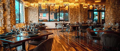 Un restaurante con suelo de madera, paredes de piedra y varias mesas dispuestas con copas de vino y platos.