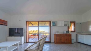 A modern living room with a TV, a sofa, a dining area with a table and chairs, a kitchen with cabinets and a microwave, and a sliding glass door leading to a balcony with a view. - Sea & Tranquility - with Wi-Fi and sea view (Olbia)