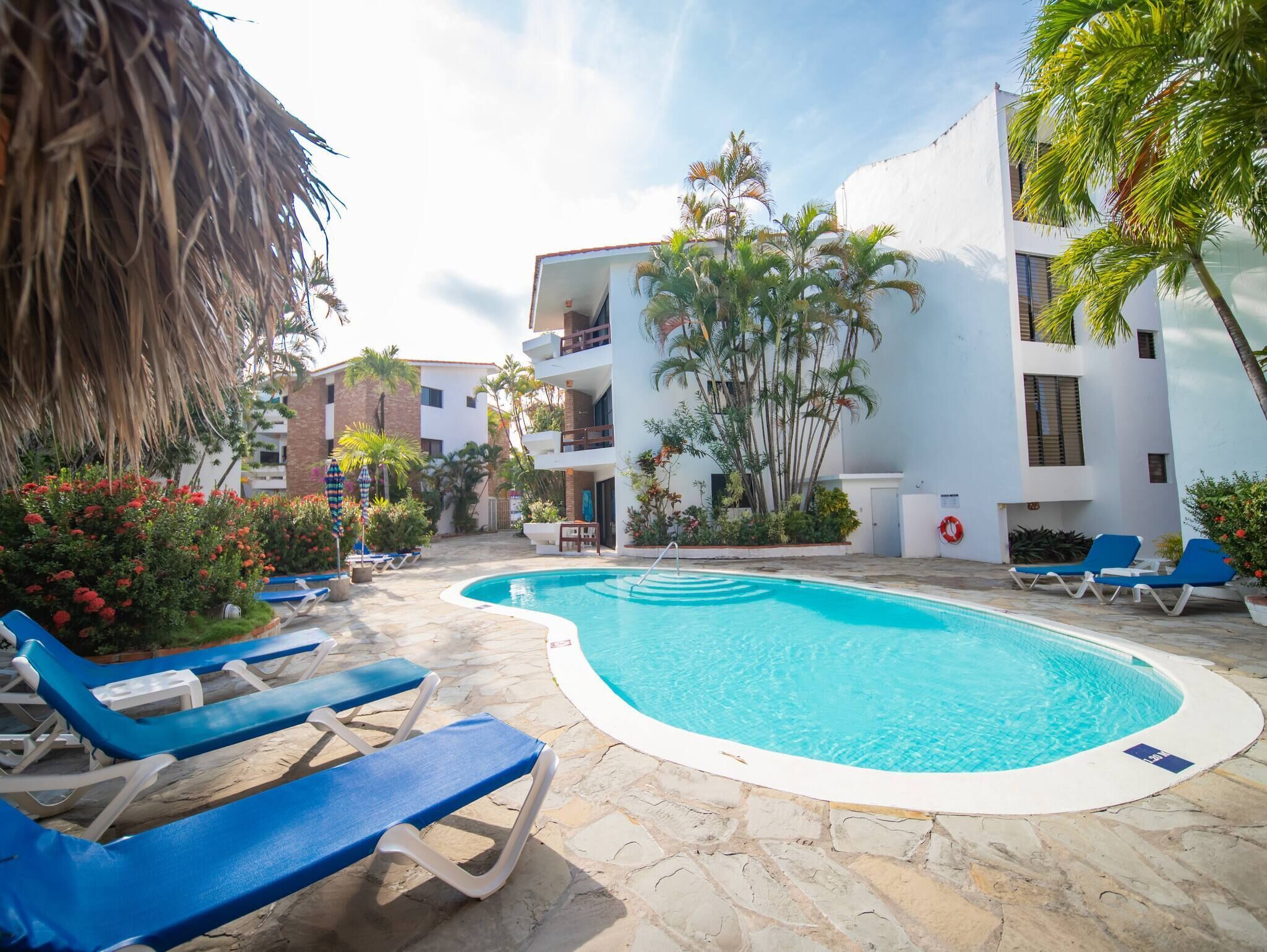 A pool area with blue lounge chairs, a clear pool, and surrounding greenery.