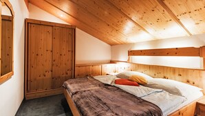 Un dormitorio con techo de madera, una cama con manta marrón, una mesita de noche y un armario.