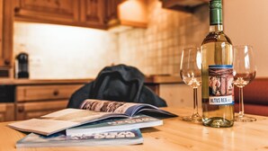 Una botella de vino Altus Rex, dos copas y una revista sobre una mesa de madera en una cocina con armarios de madera.