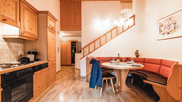 Una cocina moderna con armarios de madera, horno empotrado y un comedor con mesa redonda y sofá rojo.