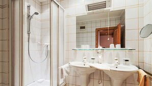 Un baño moderno con ducha de vidrio, dos lavamanos y un espejo sobre ellos.